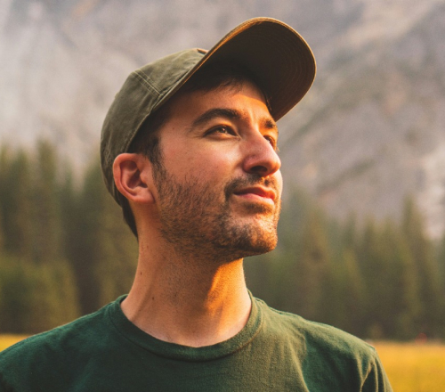 Man in a cap smiling outdoors in a mountain meadow
